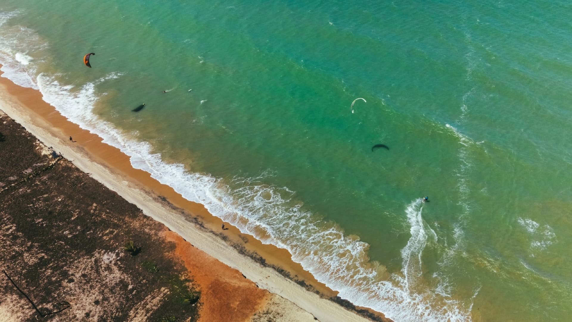 An aerial view of a kitesurfer on turquoise water along a remote sandy beach in northeast Brazil