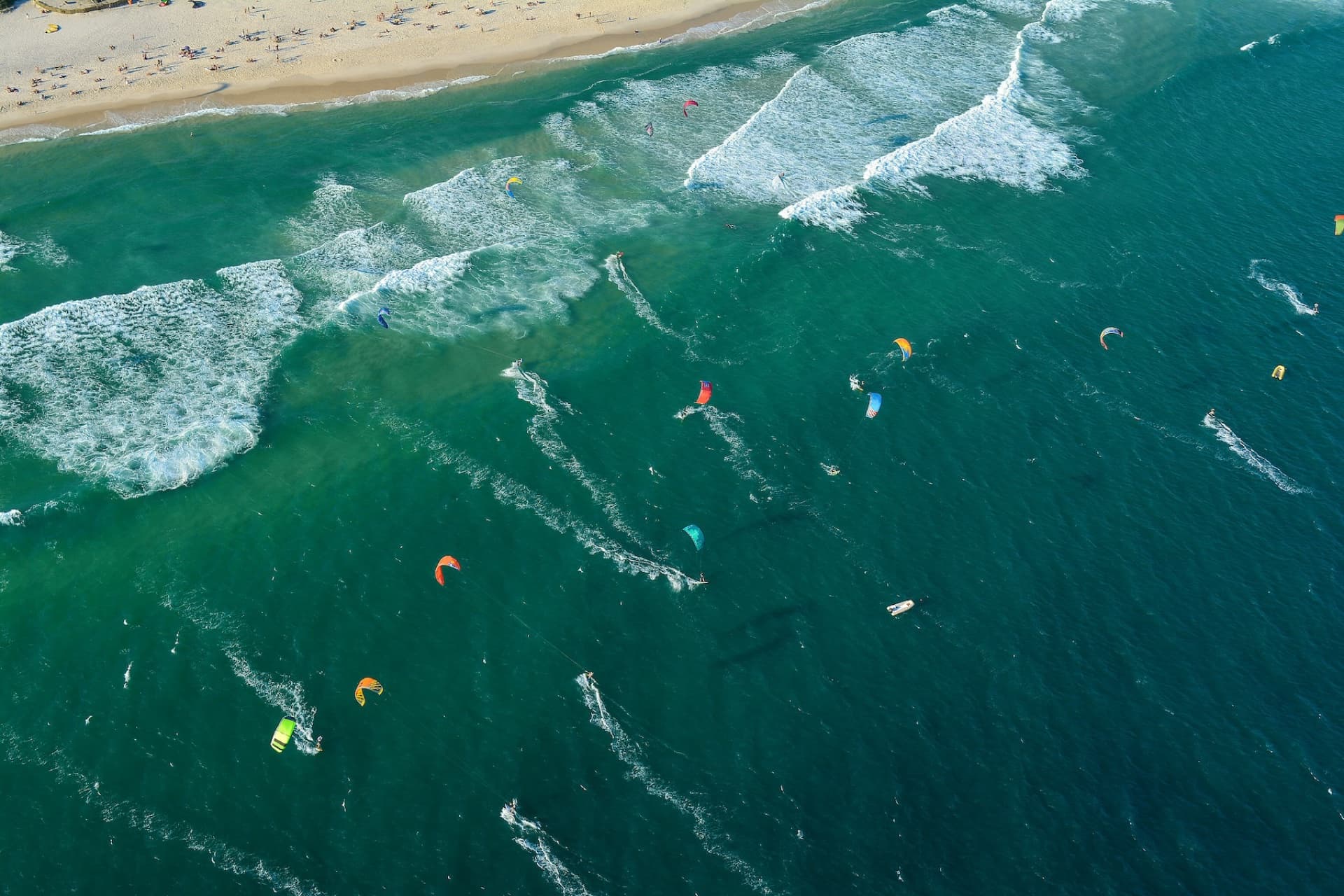 An aerial view of dozens of kitesurfers on turquoise water off a busy beach on the Ceará coast of northeast Brazil