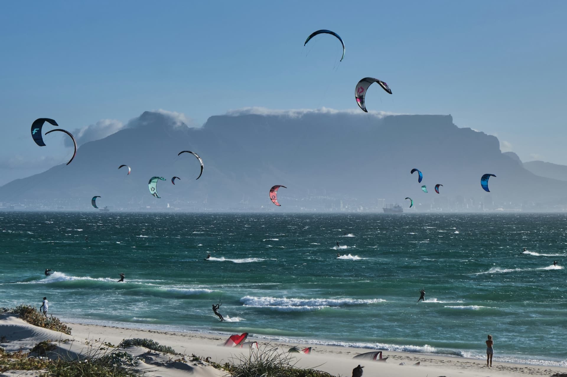 Dozens of kitesurfers at Bloubergstrand with Table Mountain and its cloud tablecloth across the bay