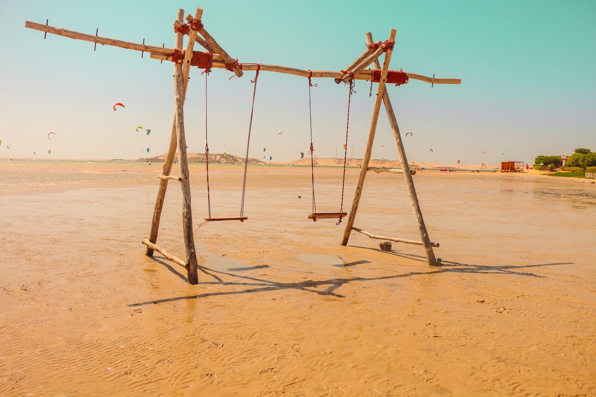 A wooden swing standing in the shallow lagoon water at Dakhla, with kites in the distance