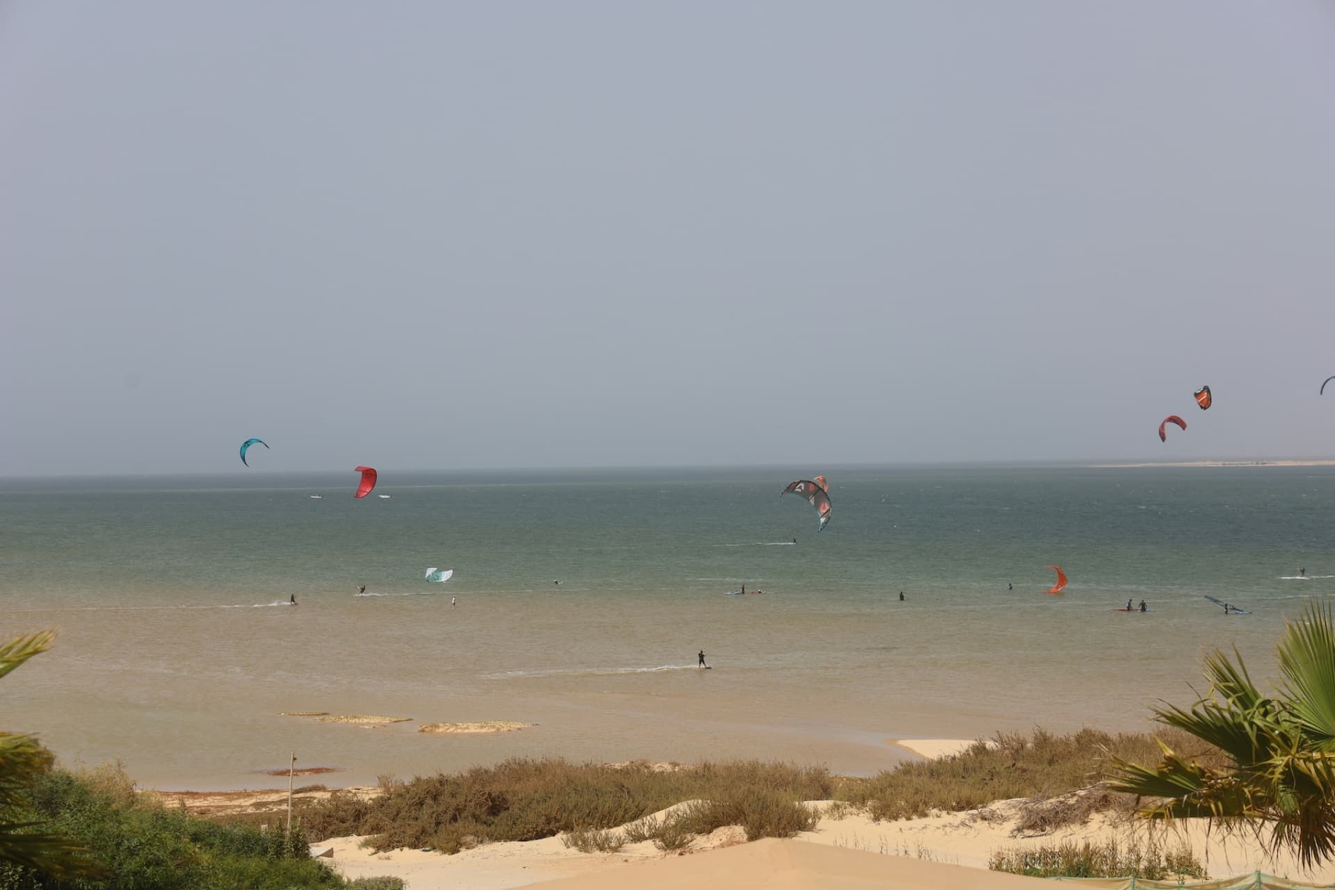 A flat turquoise lagoon in the desert with kitesurfers riding in steady wind