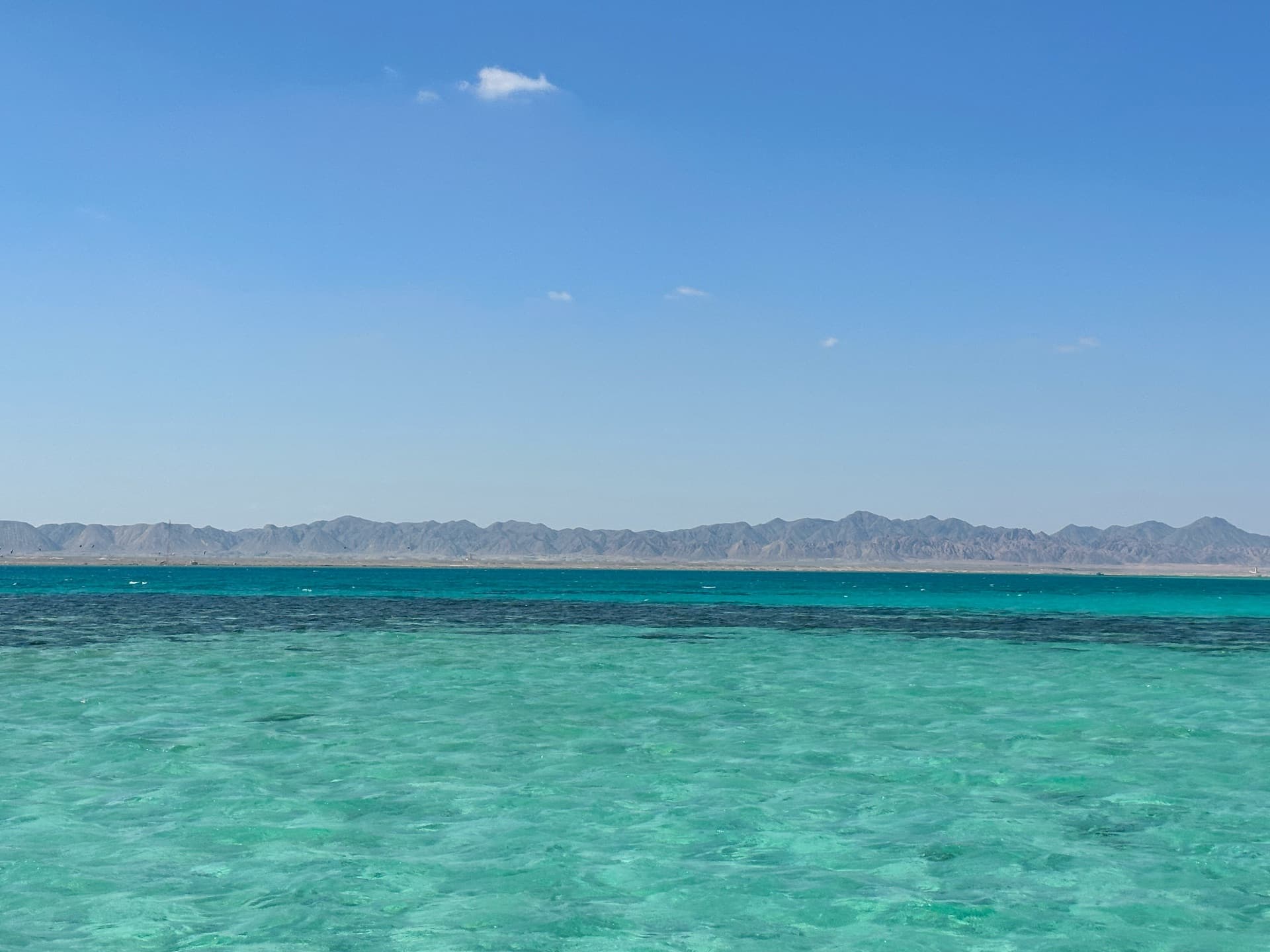 A windsurfer planing across a flat turquoise Red Sea lagoon under a steady side-shore breeze