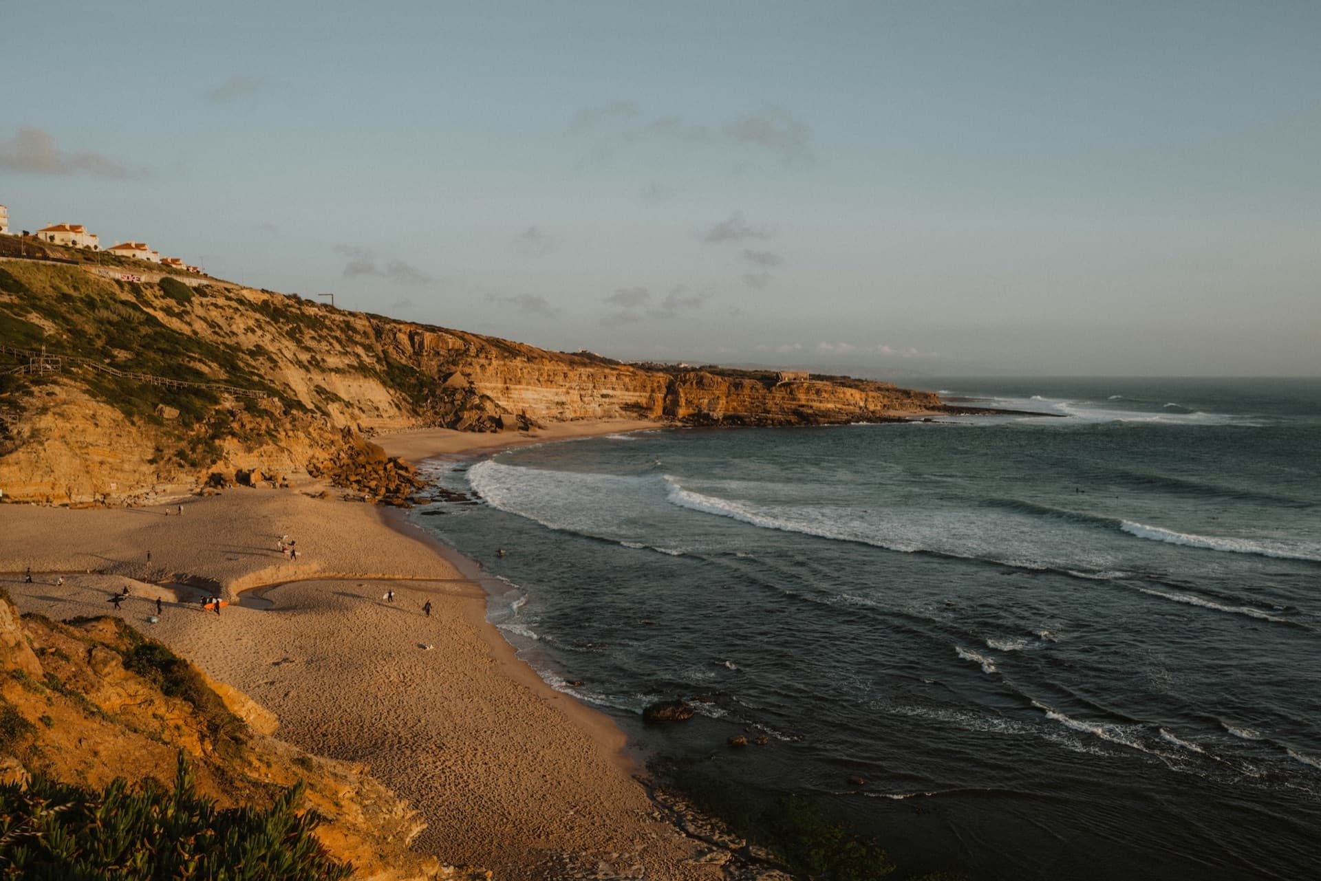 Golden-hour view over a cliff-backed beach at Ericeira with lines of swell wrapping into the cove