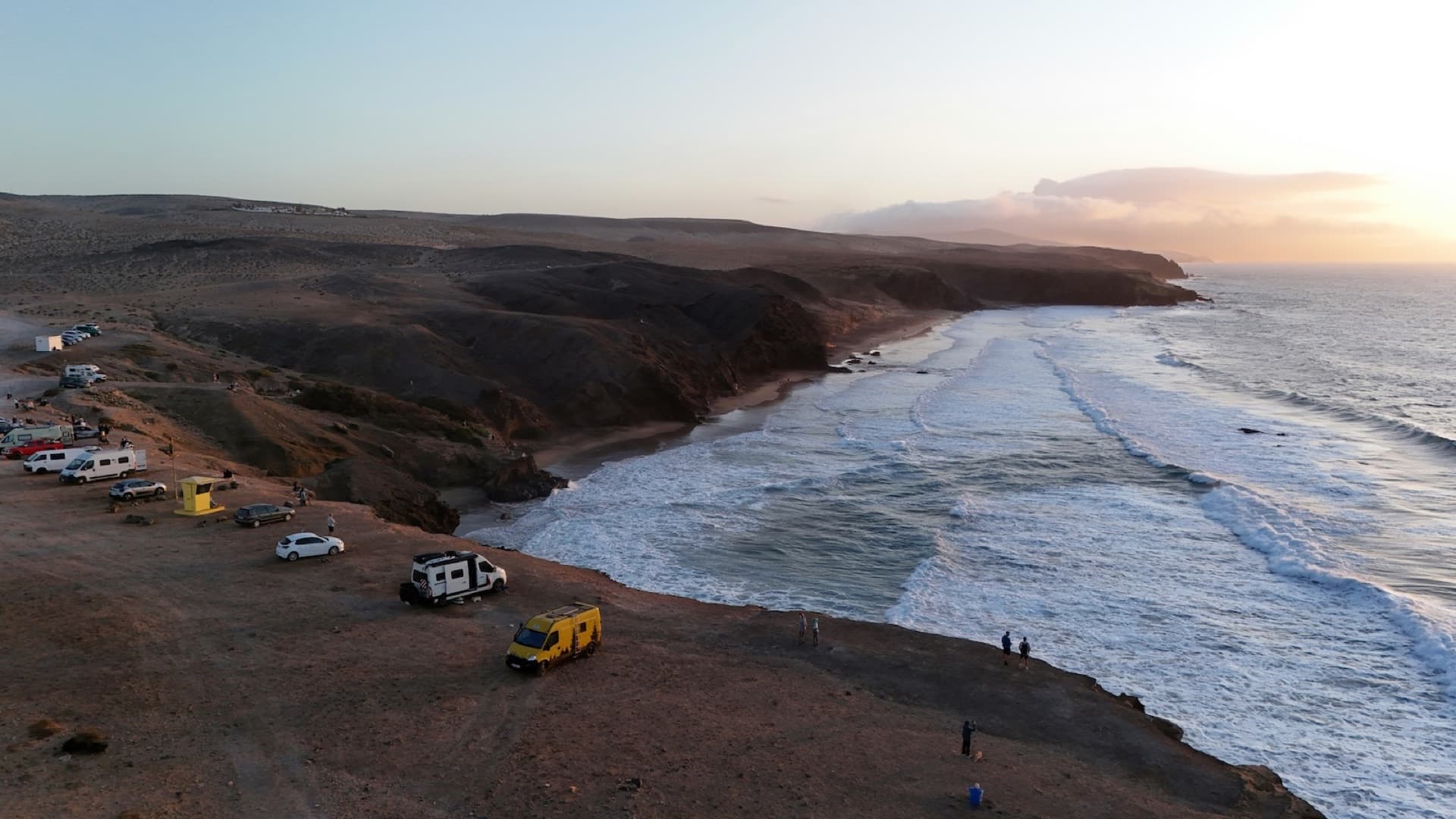 Campervans on a cliff above a wild beach with breaking waves on Fuerteventura's west coast at sunset
