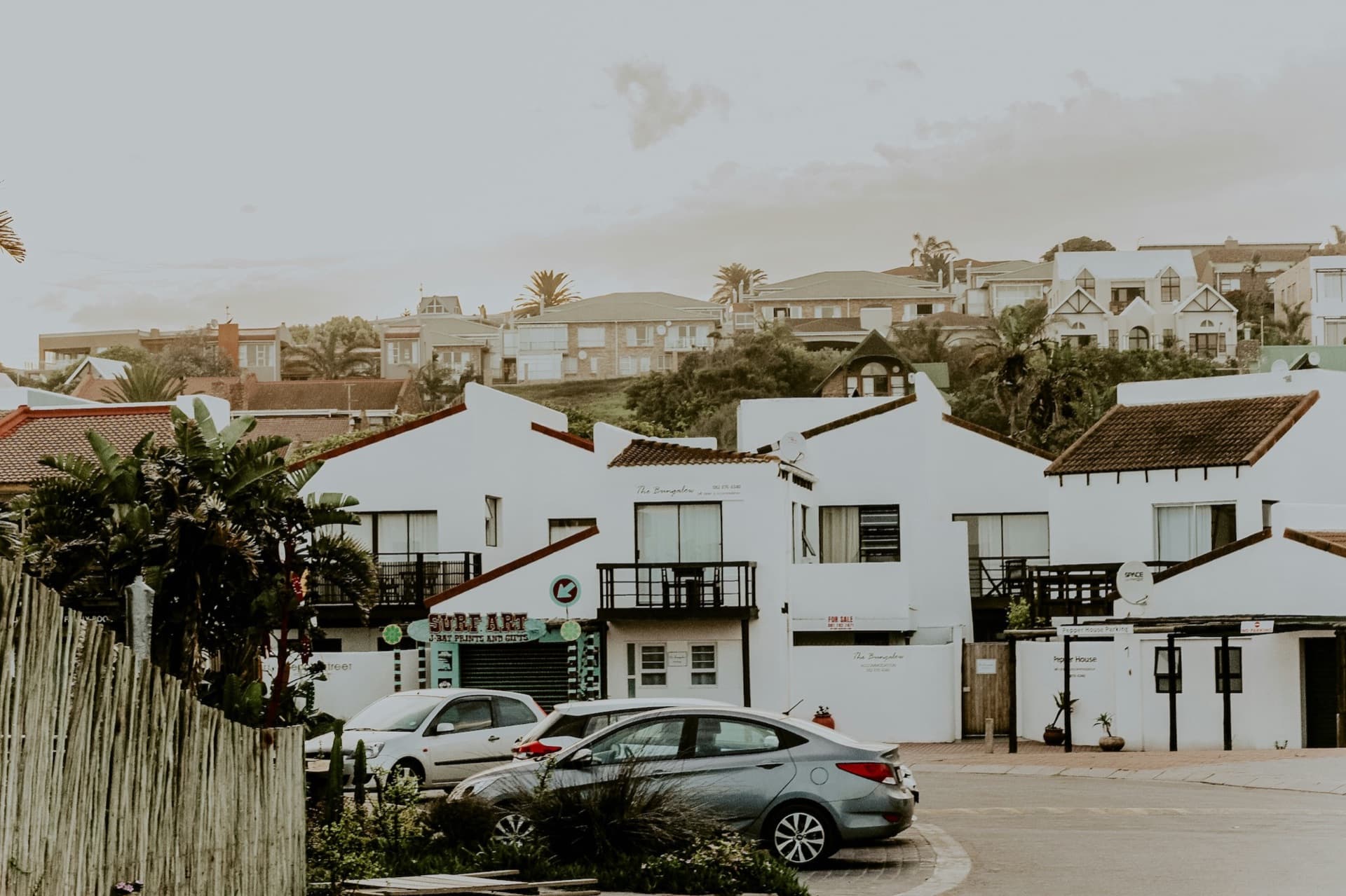 A street in Jeffreys Bay town with a surf shop and white beach houses on the hillside behind