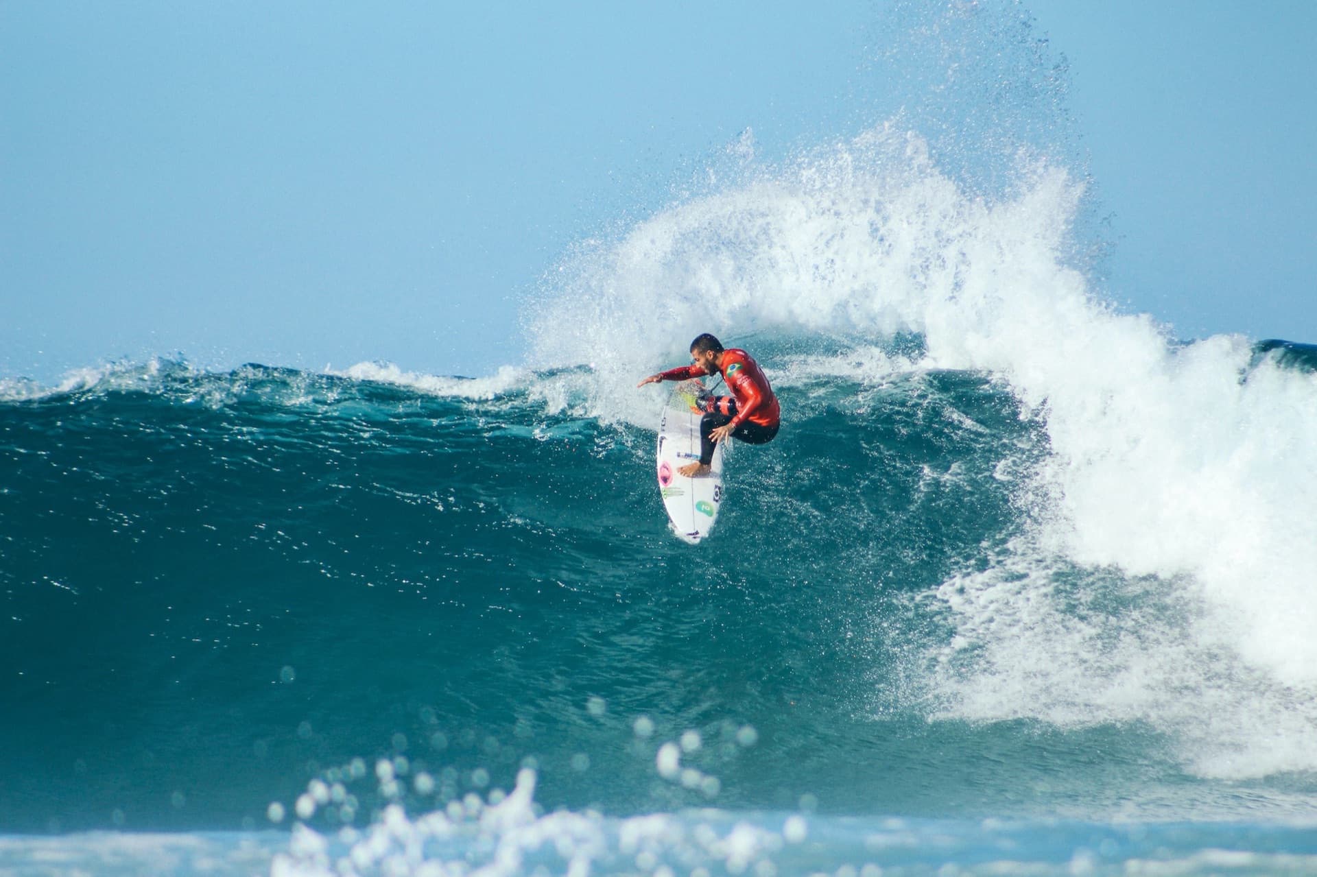 A surfer hitting the lip in a competition jersey at Jeffreys Bay, spray flying off the wave