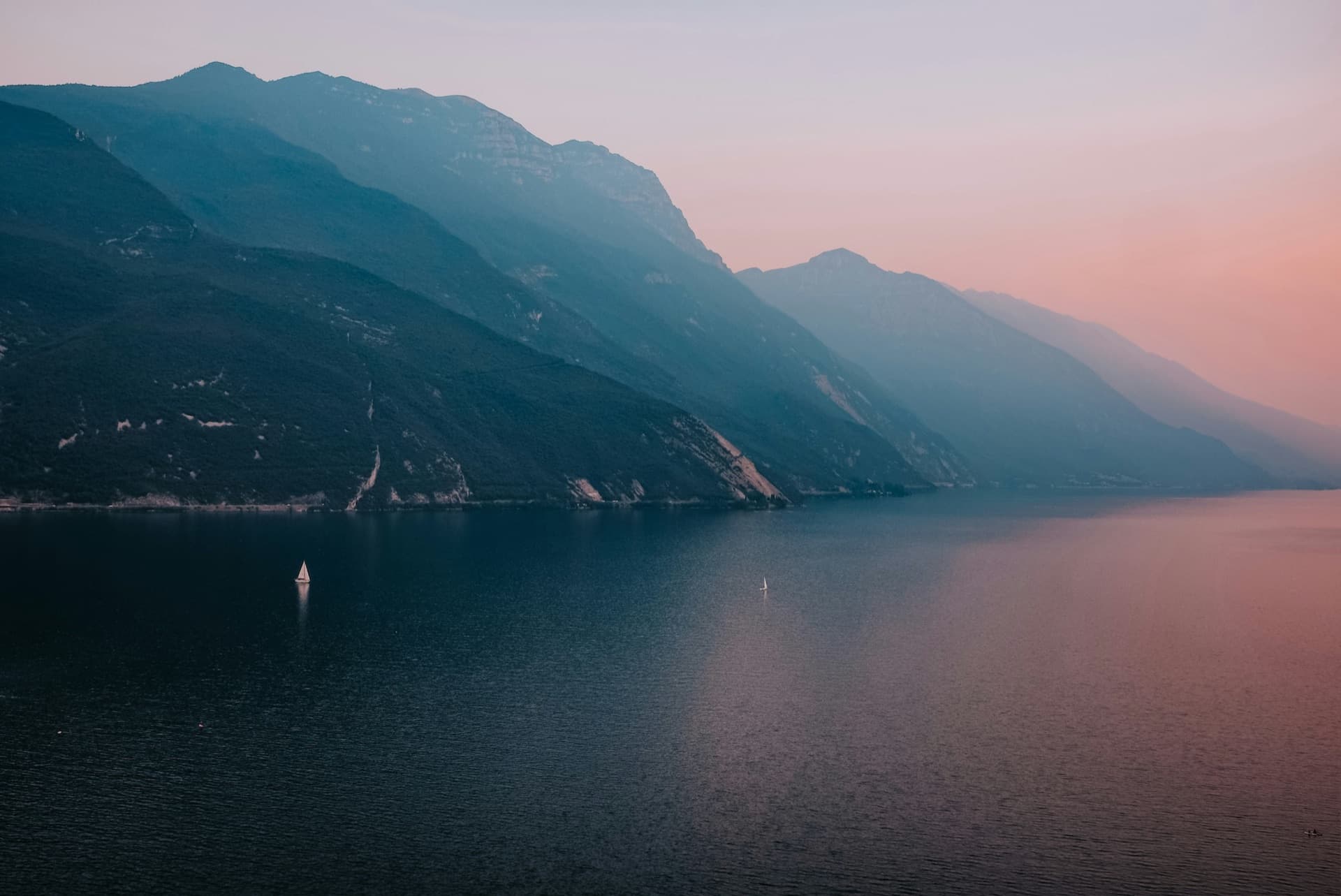 Windsurfers planing across Lake Garda below steep Alpine cliffs on a sunny afternoon