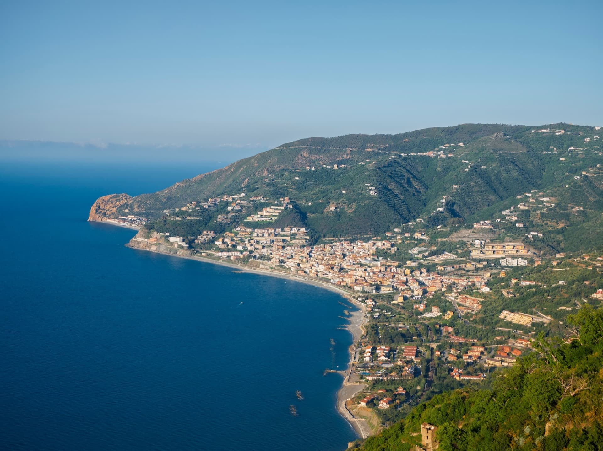 A hillside town above a curved beach and headland on the Sicilian coast