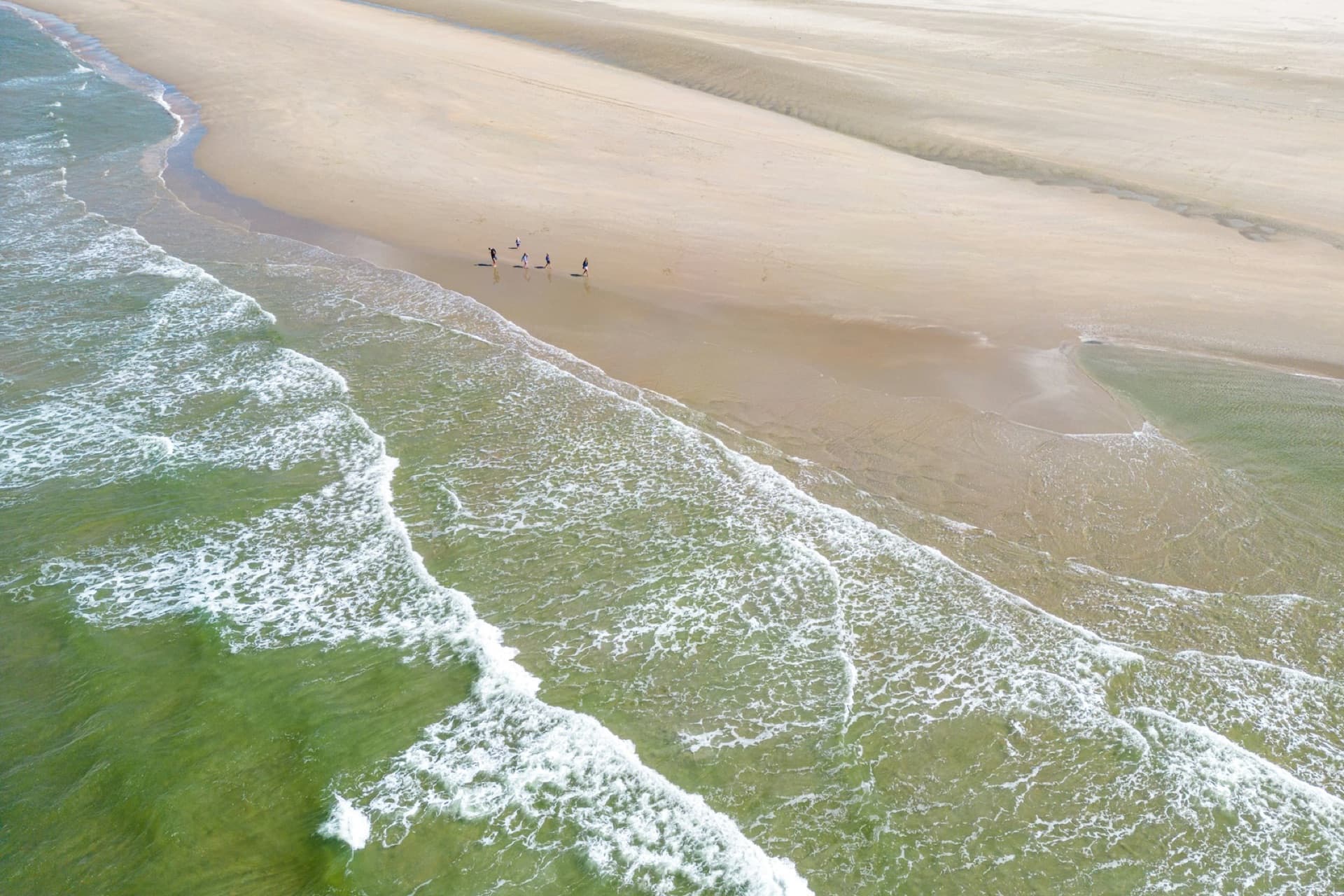 An aerial view of waves breaking on a wide sandy North Sea beach on the Dutch coast