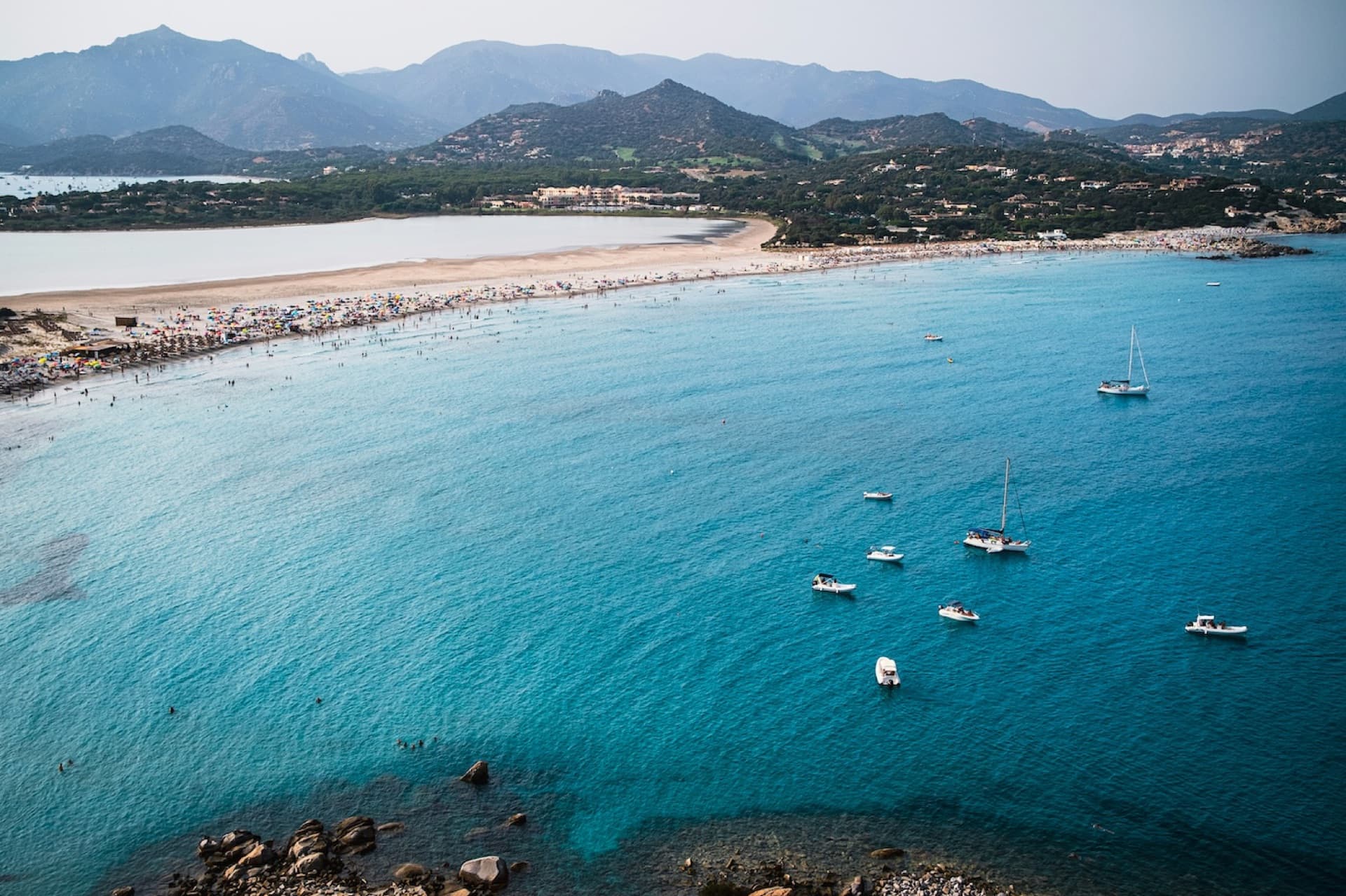 A turquoise bay with a white sand beach and anchored boats on the Sardinian coast