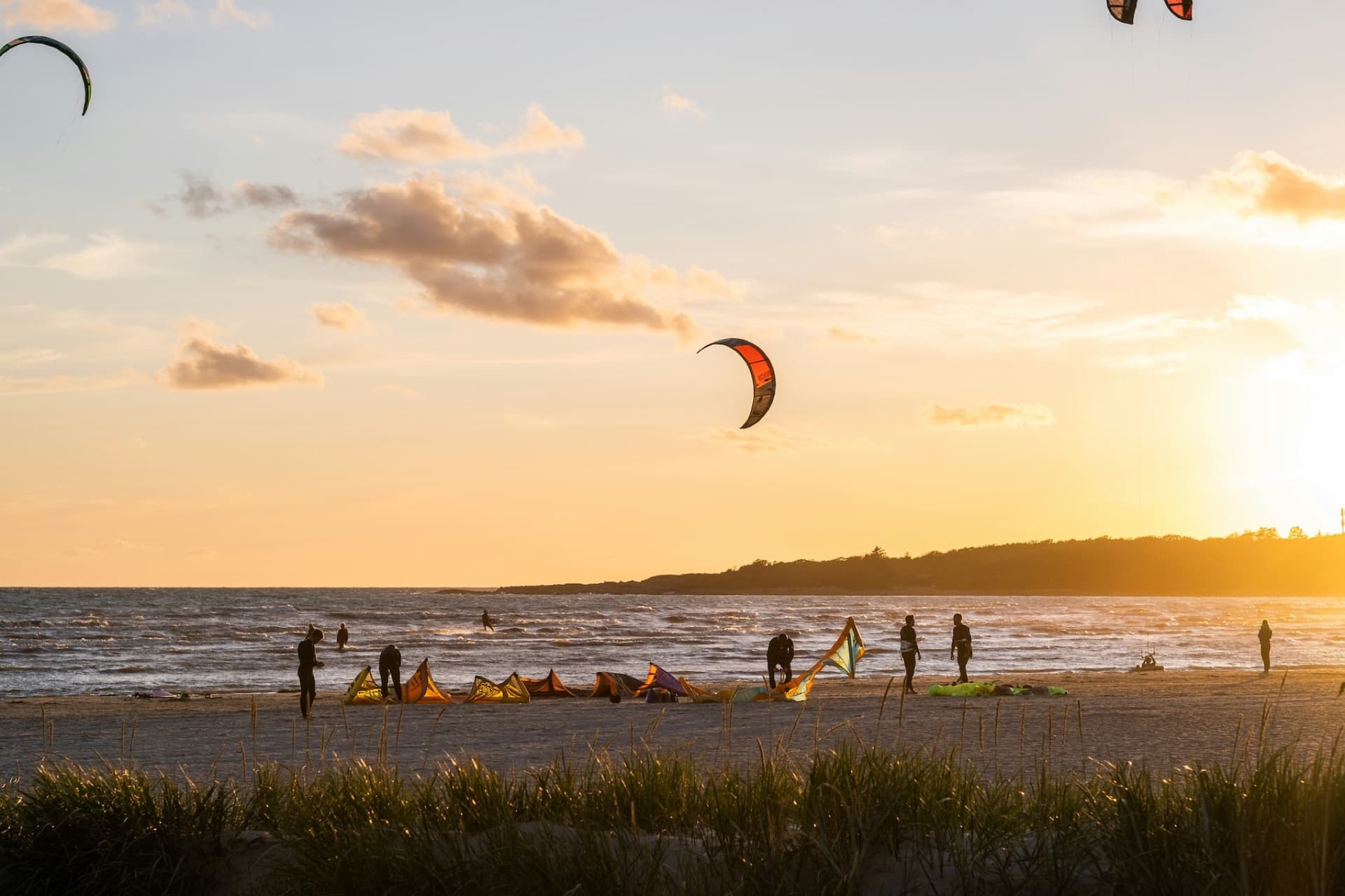Kitesurfers rigging up on a French beach at sunset with kites in the sky