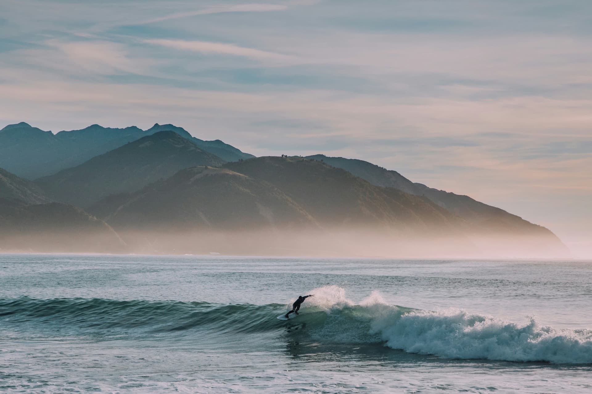 A clean ocean wave peeling under light offshore wind, spray feathering off the lip against a blue sky