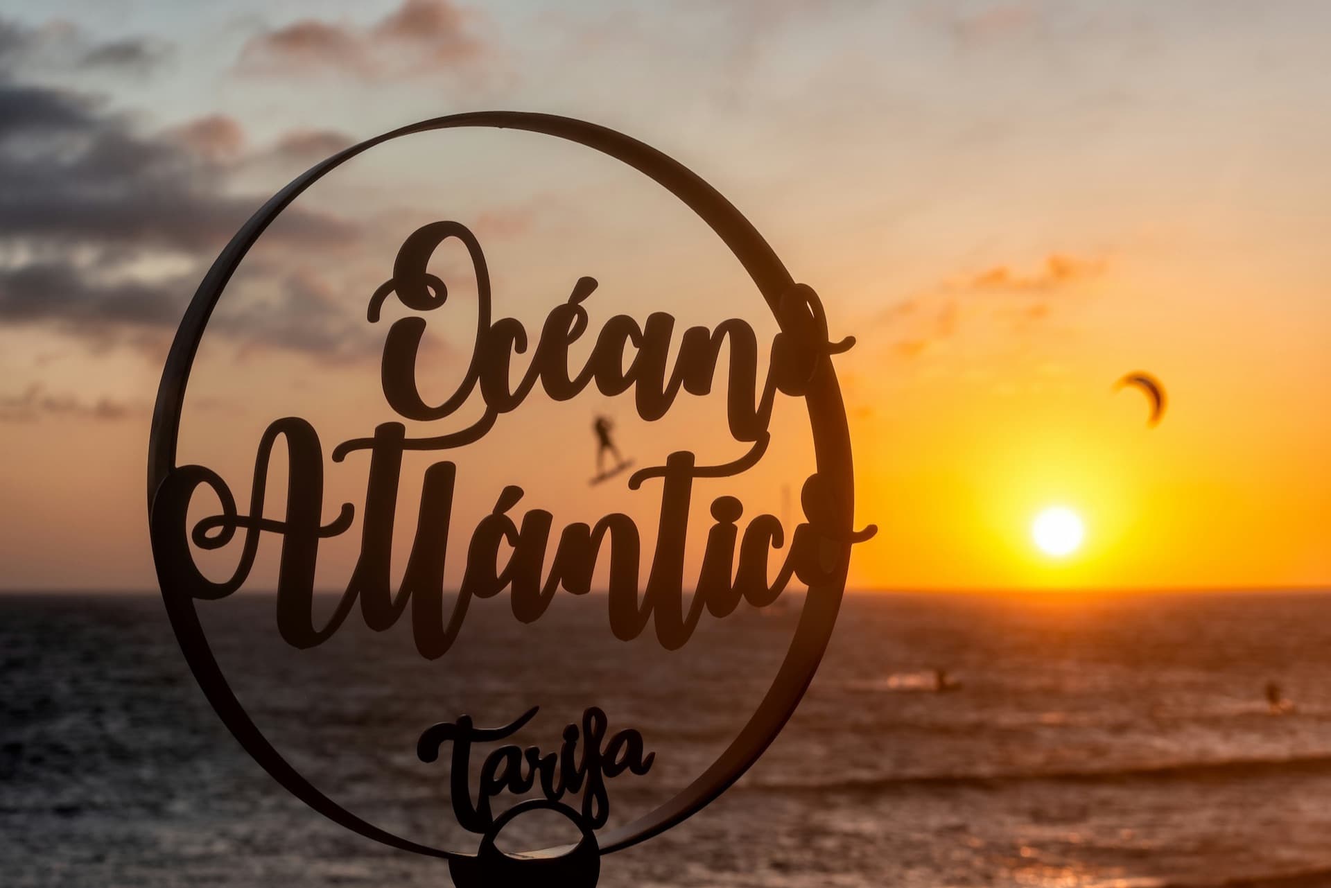 The Atlantic at Tarifa at sunset, framed by an 'Océano Atlántico' ring, with a kitesurfer in the distance