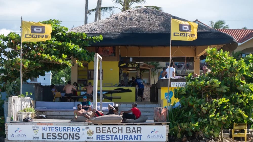 A beachfront kite school and bar at Cabarete with kite-brand flags flying and riders relaxing on the sand