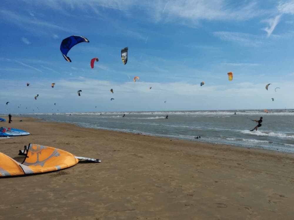 Wide firm sand and shallow water at Camber Sands with kitesurfers and dunes behind