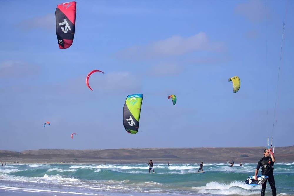 Multiple kitesurfers riding cross-onshore waves under a sky full of kites at Kite Beach on Sal